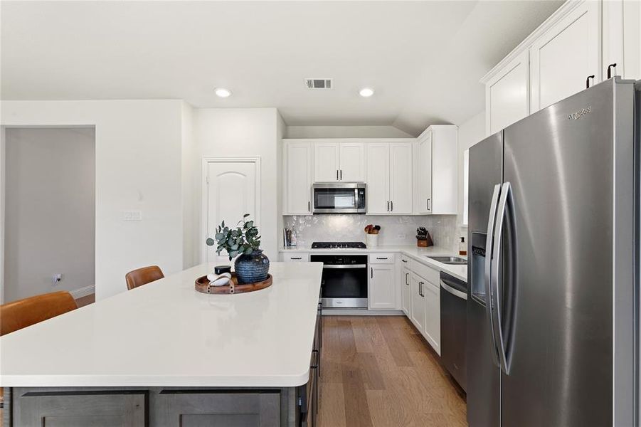 Kitchen featuring a spacious island with a light-toned countertop, white cabinetry, stainless steel appliances, and wood-finish flooring