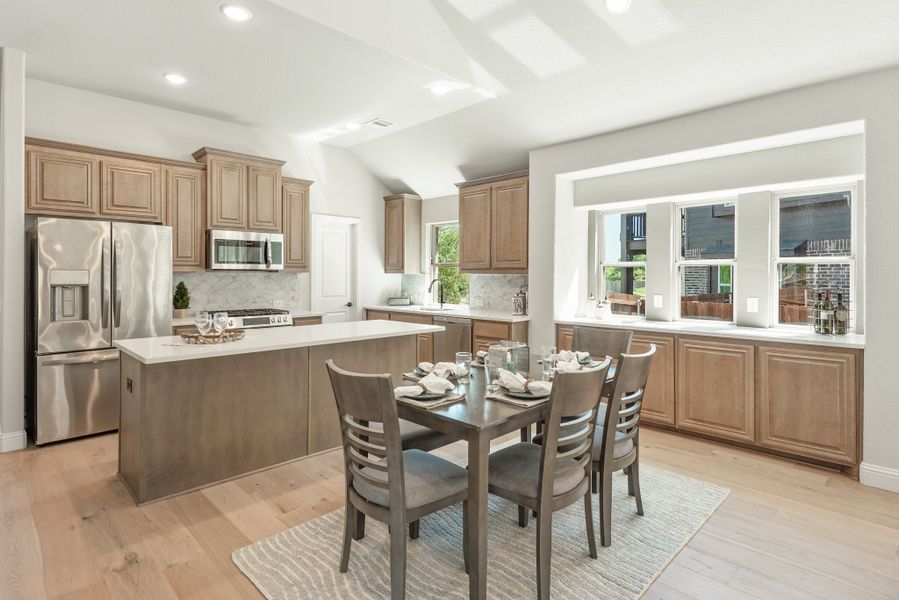 Kitchen and dining area with wood cabinets, center island, stainless appliances, and four-seat dining table on light hardwood floors
