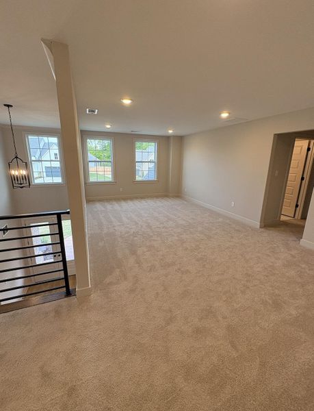 Spacious carpeted room featuring multiple windows, recessed lighting, and a modern black metal railing