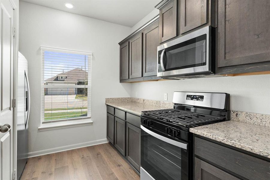 Kitchen with stainless steel appliances, light stone countertops, light wood-style floors, dark brown cabinets, and recessed lighting