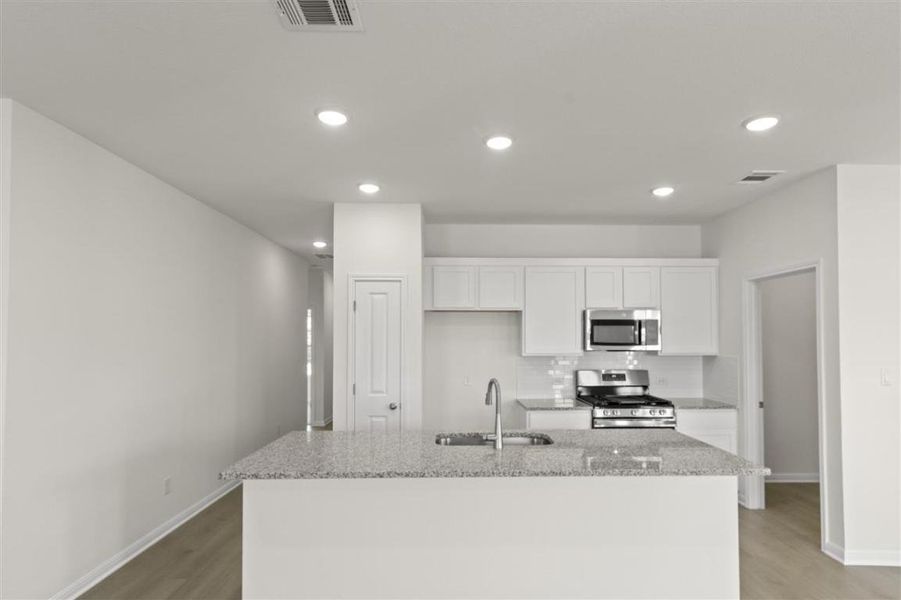 Kitchen featuring stainless steel appliances, visible vents, light wood-style floors, white cabinetry, and a sink