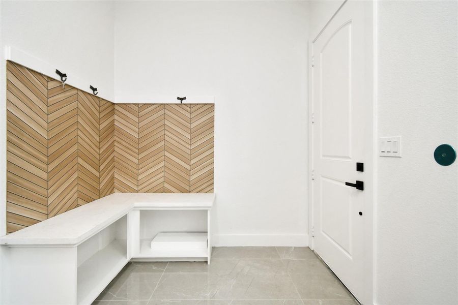 Functional elegance in the mudroom featuring a built-in bench and a beautiful wood-look chevron tile backsplash.