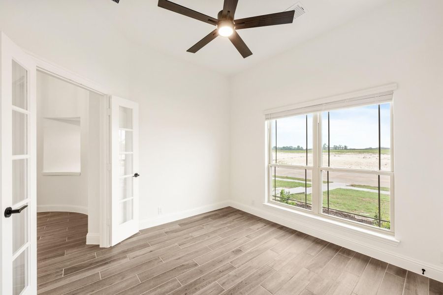 Empty bedroom with wood-look tile floors, ceiling fan, large window, and French doors leading to adjacent room
