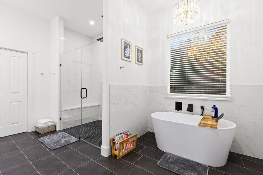 Bathroom with a marble finish shower, a soaking tub, and a chandelier