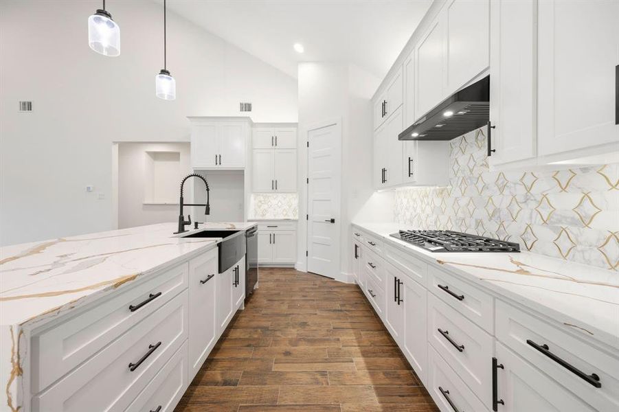 Kitchen featuring white shaker cabinetry, gold-veined countertops, wood-finish flooring, a black farmhouse sink, and geometric tile backsplash Kitchen featuring white shaker cabinetry, gold-veined countertops, wood-finish flooring, a black farmhouse sink, and geometric tile backsplash