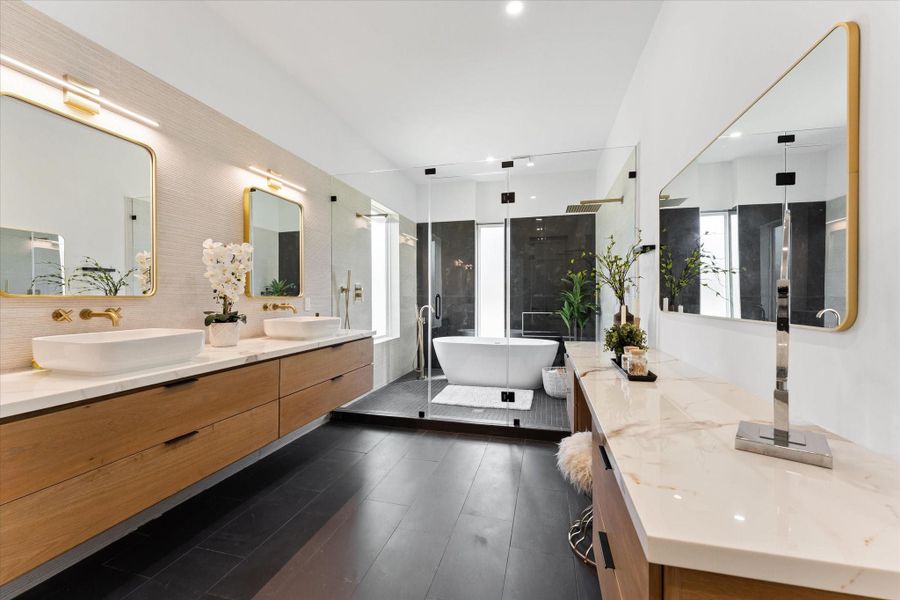 This modern primary bathroom features a sleek design with dual vessel sinks, elegant gold fixtures, and a spacious glass-enclosed shower. The freestanding bathtub adds a luxurious touch, while the natural light enhances the contemporary aesthetic. This modern primary bathroom features a sleek design with dual vessel sinks, elegant gold fixtures, and a spacious glass-enclosed shower. The freestanding bathtub adds a luxurious touch, while the natural light enhances the contemporary aesthetic.