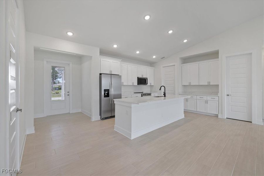 Kitchen featuring vaulted ceiling, appliances with stainless steel finishes, white cabinetry, light wood-style flooring, and recessed lighting