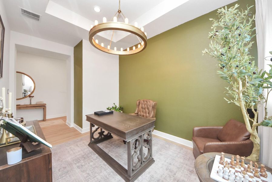Elegant home office featuring a sophisticated desk, plush leather chair, and a stylish chandelier against a warm green accent wall, perfect for work or study.