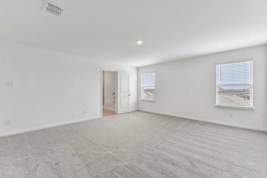 Spacious room featuring light gray carpeting, neutral wall paint, two windows with blinds, a recessed ceiling light, and an open doorway revealing a bathtub