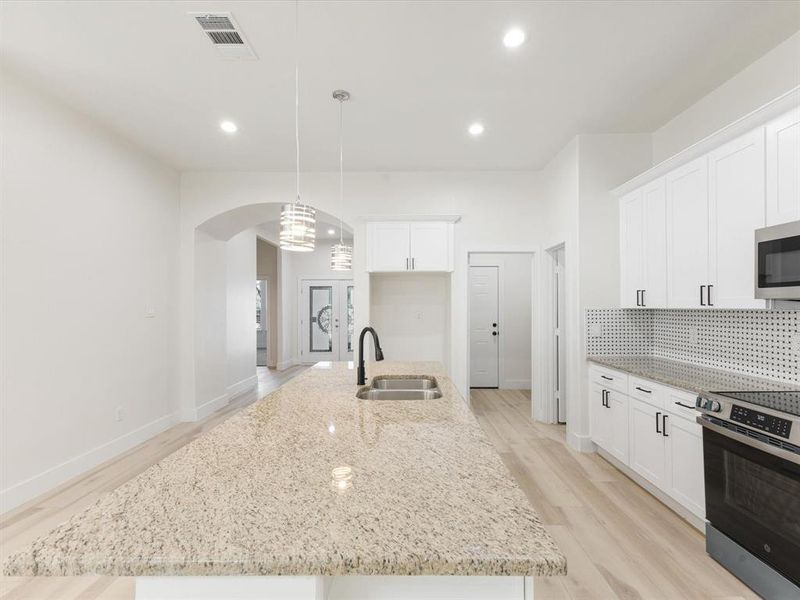 Kitchen featuring light stone counters, appliances with stainless steel finishes, a kitchen island with sink, white cabinetry, and hanging light fixtures