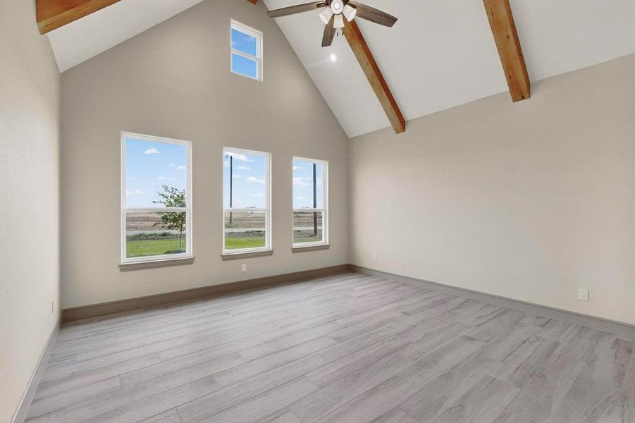 Empty room with high vaulted ceiling, beam ceiling, light wood-style floors, and a ceiling fan Empty room with high vaulted ceiling, beam ceiling, light wood-style floors, and a ceiling fan