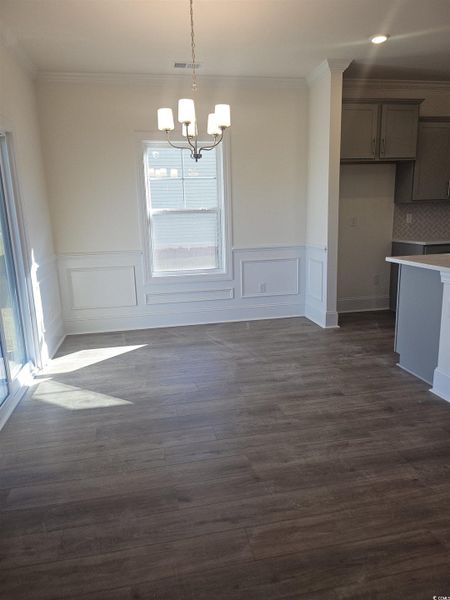 Unfurnished dining area with crown molding, a chandelier, dark wood-style flooring, wainscoting, and a decorative wall