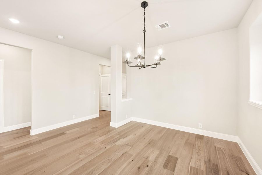 Empty dining room with light hardwood floors, white walls, and a black metal chandelier