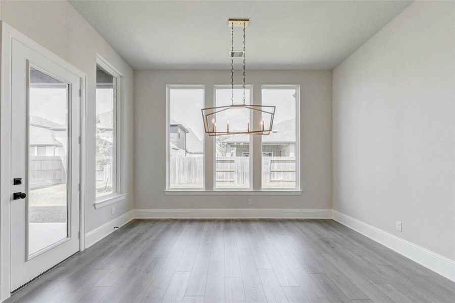 This dining room features large windows that provide ample natural light, a modern chandelier, and sleek flooring. French door open to a backyard, enhancing the space's airy, open feel.
