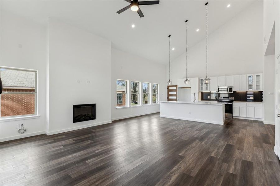 Unfurnished living room featuring high vaulted ceiling, dark hardwood / wood-style floors, and ceiling fan