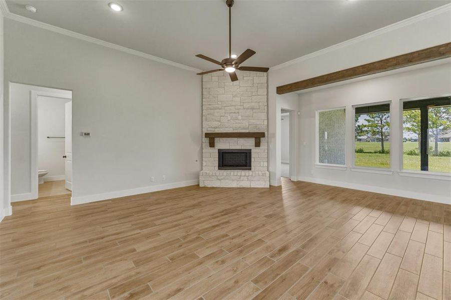 Spacious living area featuring light wood-finish flooring, a stone-clad fireplace with a dark wood mantel, and a ceiling fan Spacious living area featuring light wood-finish flooring, a stone-clad fireplace with a dark wood mantel, and a ceiling fan