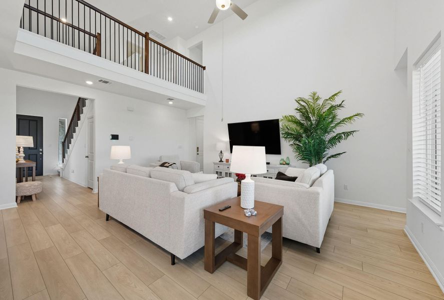 Living room featuring a towering ceiling, light wood finished floors, a ceiling fan, and stairs Living room featuring a towering ceiling, light wood finished floors, a ceiling fan, and stairs