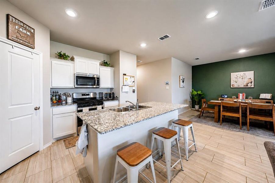 Kitchen featuring white cabinetry, stainless steel appliances, and a granite-topped island with an integrated double basin sink
