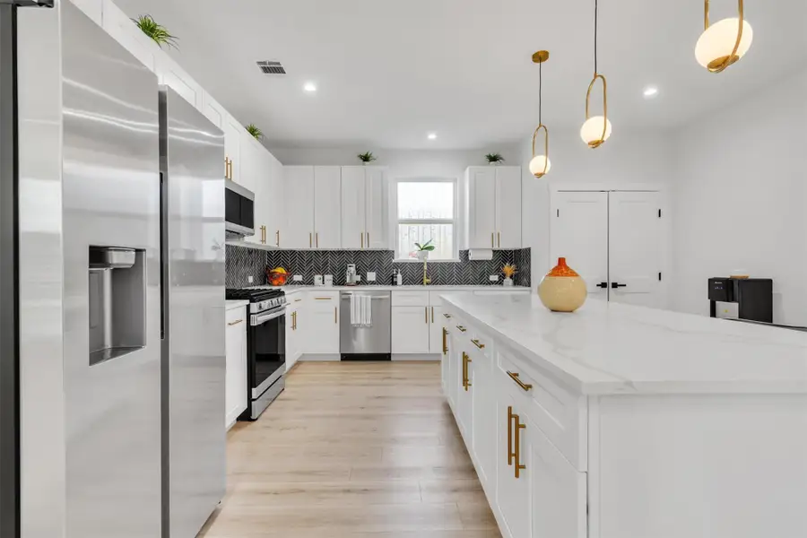 Kitchen featuring stainless steel appliances, hanging light fixtures, a kitchen island, and white cabinetry