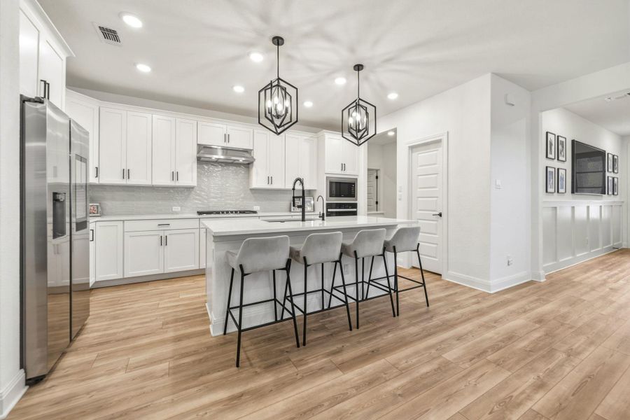 Spacious kitchen featuring white cabinetry, stainless steel appliances, a center island with seating, pendant lighting, and quartz countertops