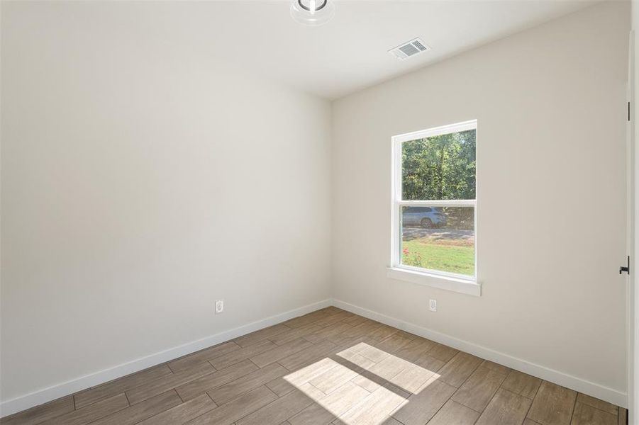 Room featuring light-toned walls, wood-finish flooring, a single double-hung window, and a modern ceiling light fixture Room featuring light-toned walls, wood-finish flooring, a single double-hung window, and a modern ceiling light fixture