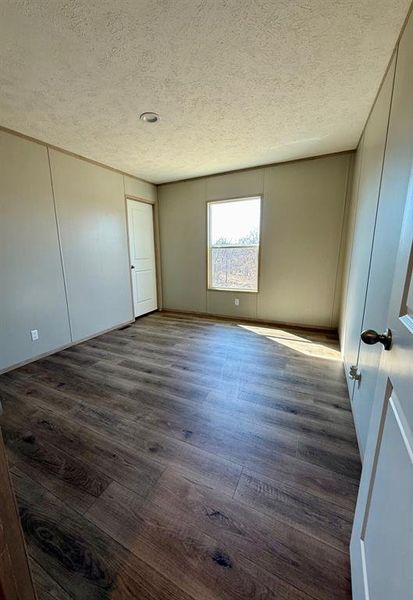 Unfurnished bedroom featuring a textured ceiling, dark wood-type flooring, and a closet Unfurnished bedroom featuring a textured ceiling, dark wood-type flooring, and a closet