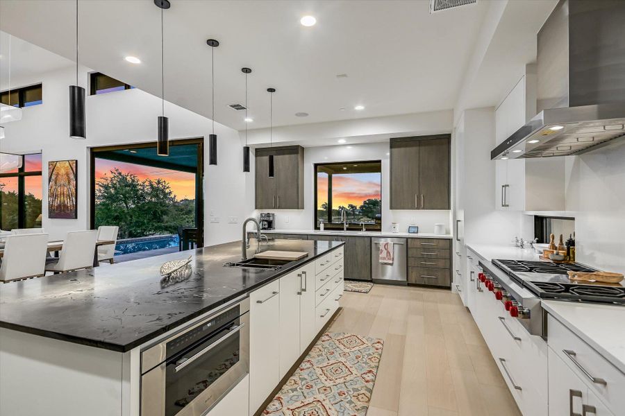 Two tone kitchen featuring two tone cabinetry, decorative light fixtures, modern cabinets, an island with sink, and stainless steel appliances Two tone kitchen featuring two tone cabinetry, decorative light fixtures, modern cabinets, an island with sink, and stainless steel appliances