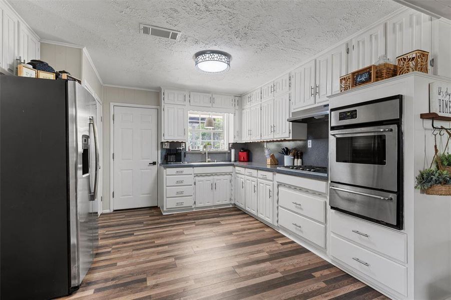 Kitchen featuring appliances with stainless steel finishes, a warming drawer, ornamental molding, a sink, and dark wood-type flooring Kitchen featuring appliances with stainless steel finishes, a warming drawer, ornamental molding, a sink, and dark wood-type flooring