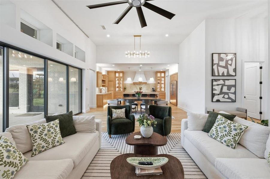 Living room with light wood-style flooring, ceiling fan, a high ceiling, and suspended lighting