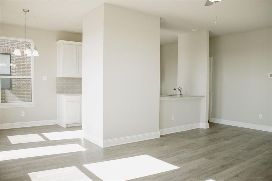 Spare room featuring ceiling fan with notable chandelier and light wood-type flooring