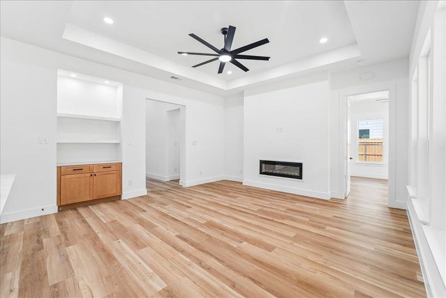 Spacious living area featuring wood-finish flooring, a contemporary linear fireplace, and built-in shelving with cabinetry Spacious living area featuring wood-finish flooring, a contemporary linear fireplace, and built-in shelving with cabinetry