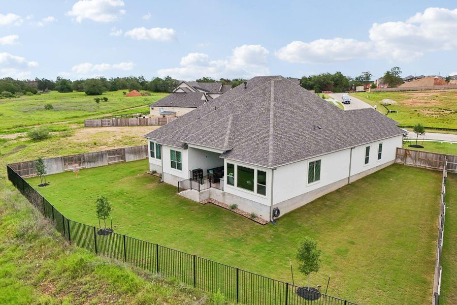 Spacious backyard featuring a manicured lawn, partial black metal fencing, and an expansive paved patio
