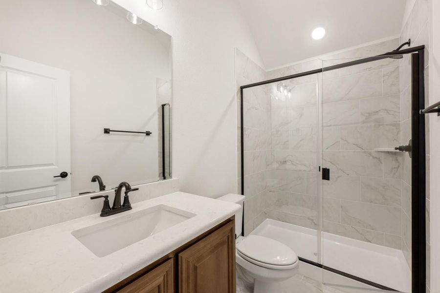 Bathroom with white quartz vanity, wood cabinets, glass shower with marble tile, and black fixtures