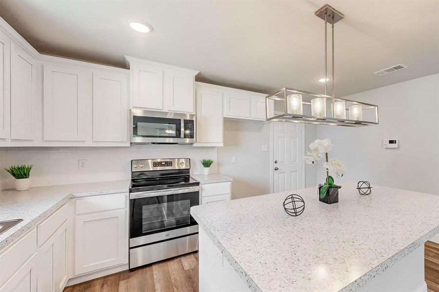 Kitchen featuring white cabinets, hanging light fixtures, a kitchen island, appliances with stainless steel finishes, and light hardwood / wood-style floors