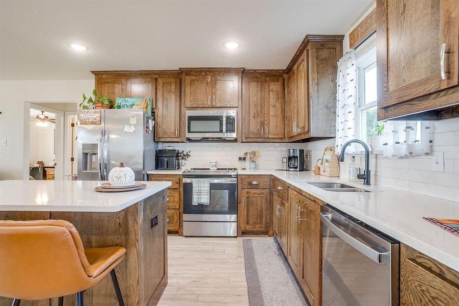 Kitchen with brown cabinets, tasteful backsplash, stainless steel appliances, light quartz countertops, and recessed lighting Kitchen with brown cabinets, tasteful backsplash, stainless steel appliances, light quartz countertops, and recessed lighting