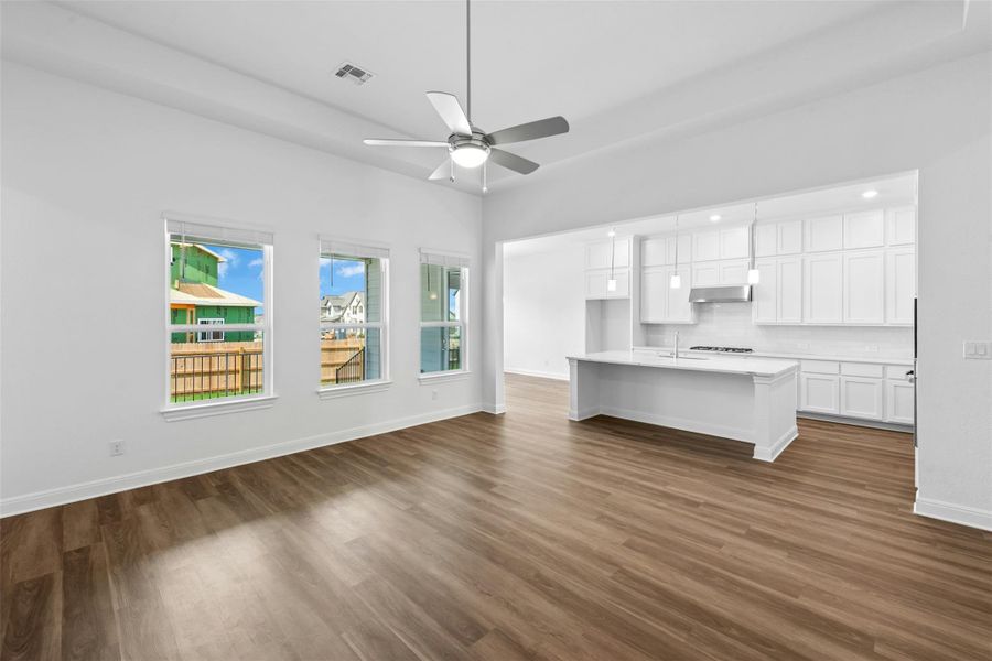 An open-concept living space presents warm wood-look flooring and a contemporary kitchen with a bright island.