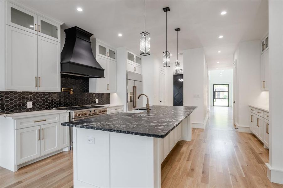 Kitchen with glass insert cabinets, tasteful backsplash, custom exhaust hood, dark stone counters, and recessed lighting Kitchen with glass insert cabinets, tasteful backsplash, custom exhaust hood, dark stone counters, and recessed lighting