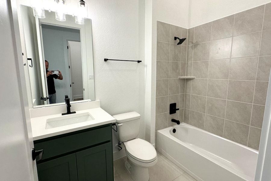 A well-appointed bathroom features a dark green vanity, modern fixtures, and a tiled shower-over-tub combination.