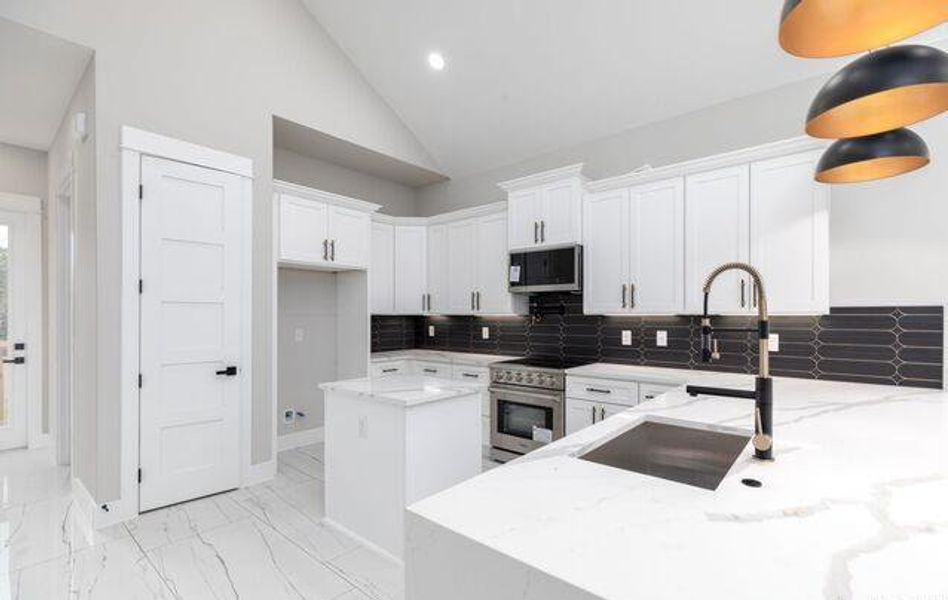 Modern kitchen featuring white cabinetry, quartz countertops, black subway tile backsplash, and stainless steel appliances