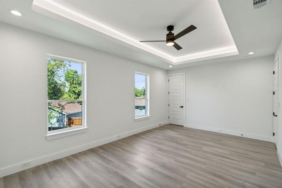 Bedroom with ceiling fan, light hardwood / wood-style floors, and a raised ceiling