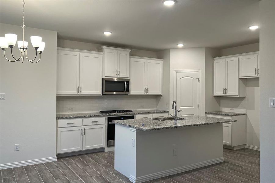 Kitchen with dark stone counters, wood tiled floors, stainless steel appliances, white cabinets, and recessed lighting Kitchen with dark stone counters, wood tiled floors, stainless steel appliances, white cabinets, and recessed lighting