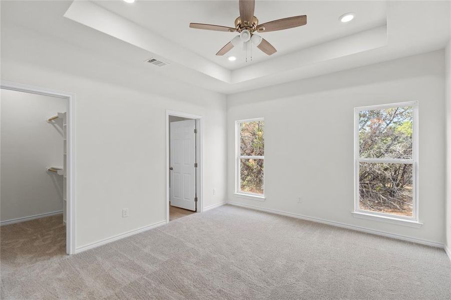 Unfurnished bedroom with a raised ceiling, light colored carpet, a walk in closet, ceiling fan, and recessed lighting Unfurnished bedroom with a raised ceiling, light colored carpet, a walk in closet, ceiling fan, and recessed lighting