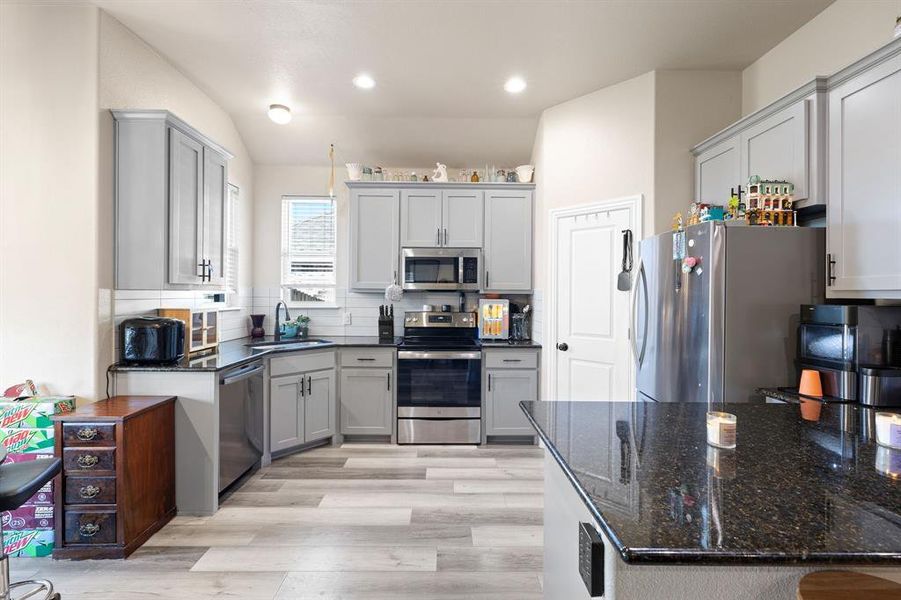 Kitchen with light wood-type flooring, tasteful backsplash, stainless steel appliances, sink, and lofted ceiling