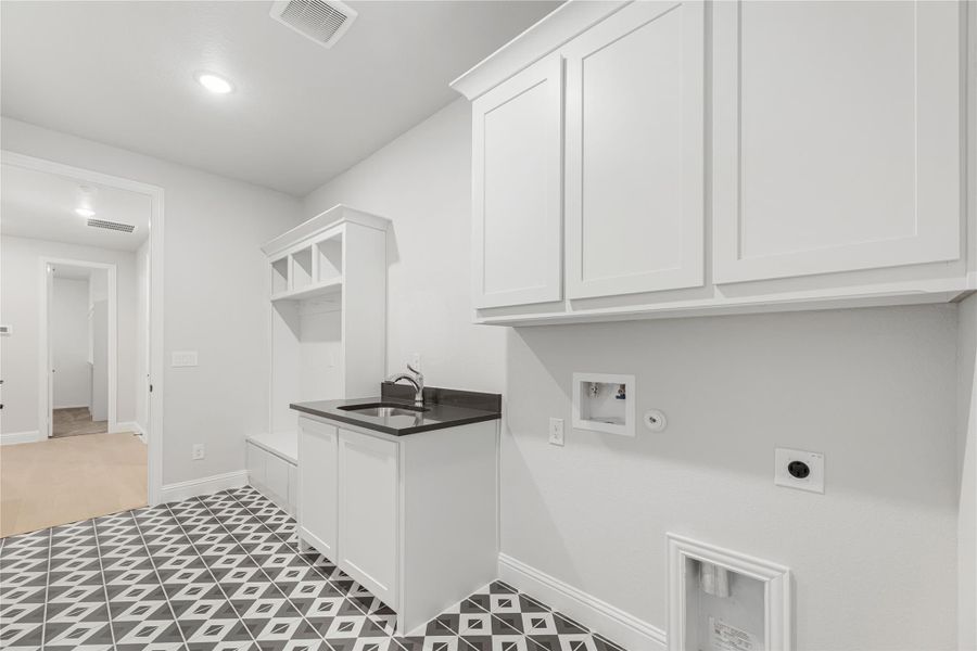 Laundry room with white cabinets, utility sink, washer hookups, and black-and-white patterned tile floor.