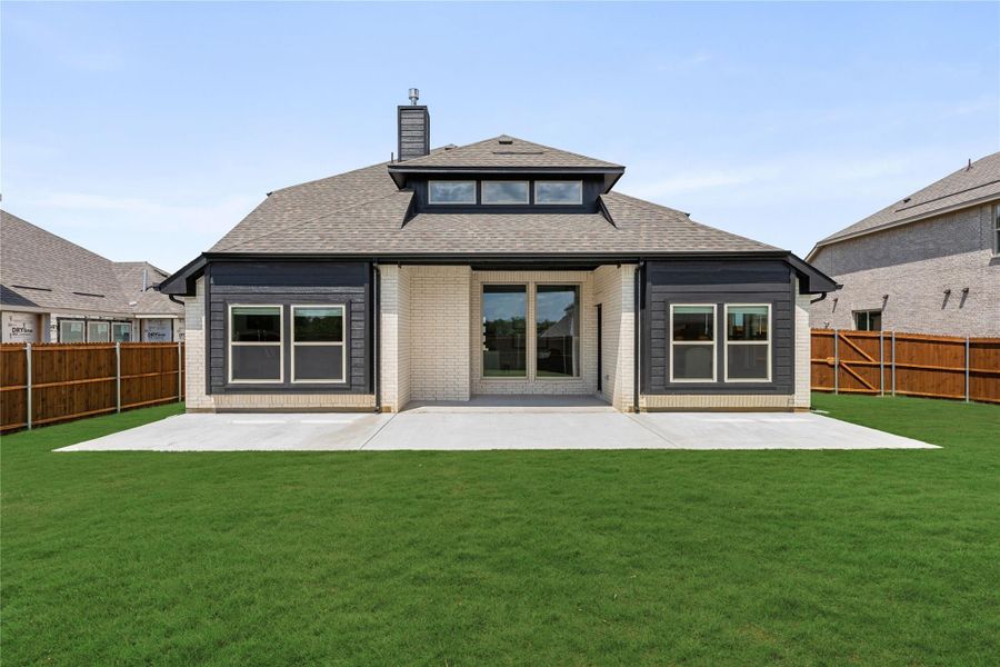 Rear exterior of single-story home with brick and dark siding, concrete patio, and fenced backyard with green lawn.