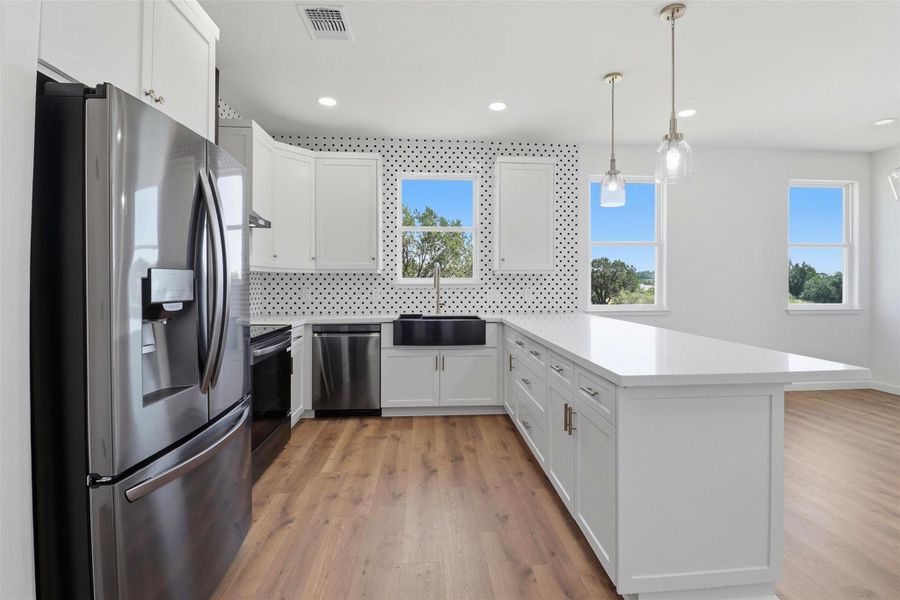 Modern kitchen featuring white shaker cabinetry, stainless steel appliances, a black farmhouse sink, and wood-finish flooring Modern kitchen featuring white shaker cabinetry, stainless steel appliances, a black farmhouse sink, and wood-finish flooring