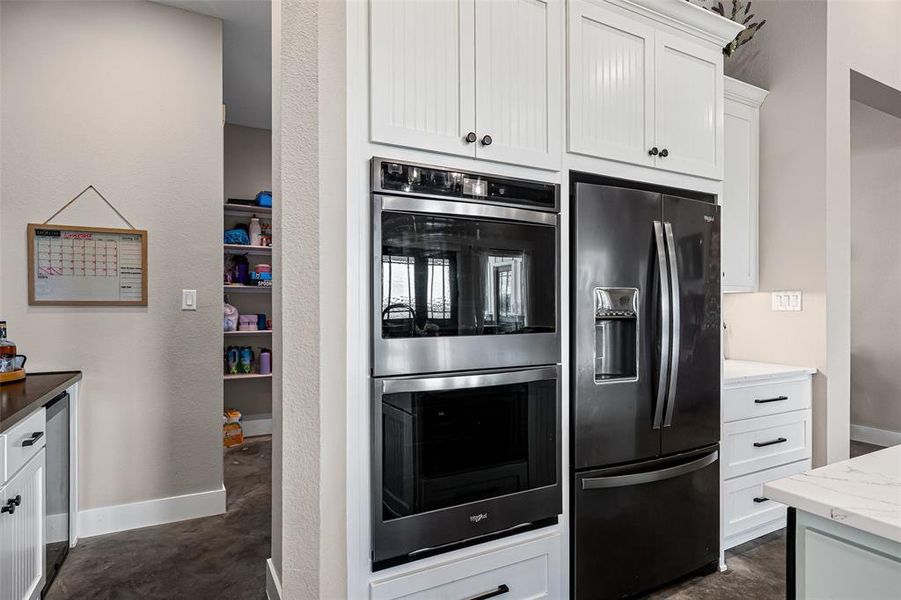 Kitchen featuring double oven, white cabinets, black fridge, light stone counters, and wine cooler Kitchen featuring double oven, white cabinets, black fridge, light stone counters, and wine cooler