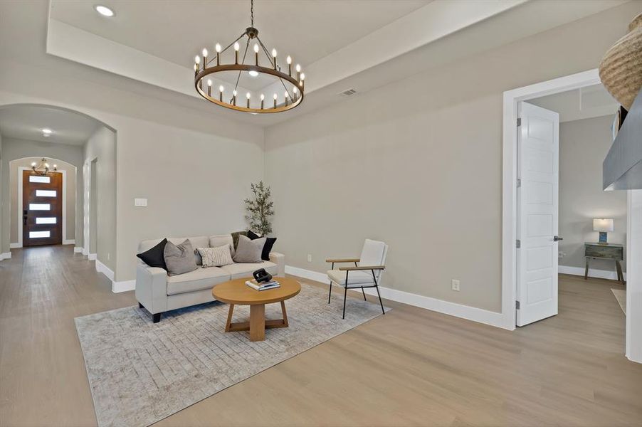Living area featuring a chandelier, arched walkways, a raised ceiling, light wood-style flooring, and baseboards