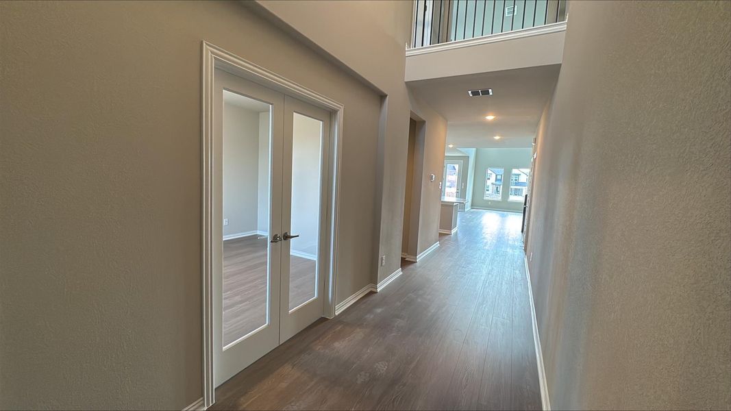 Hallway featuring french doors, a textured wall, dark wood-style flooring, and a high ceiling