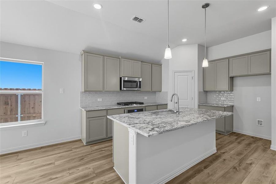 Kitchen with light stone countertops, gray cabinetry, pendant lighting, appliances with stainless steel finishes, and tasteful backsplash Kitchen with light stone countertops, gray cabinetry, pendant lighting, appliances with stainless steel finishes, and tasteful backsplash